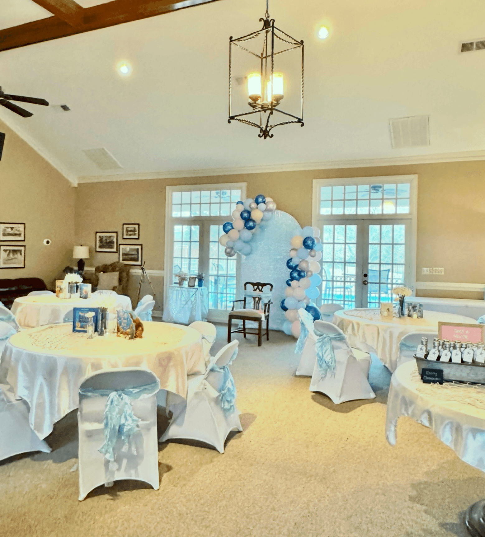Event room with round tables decorated with white tablecloths and light blue chair sashes, balloon arch backdrop, and large windows.