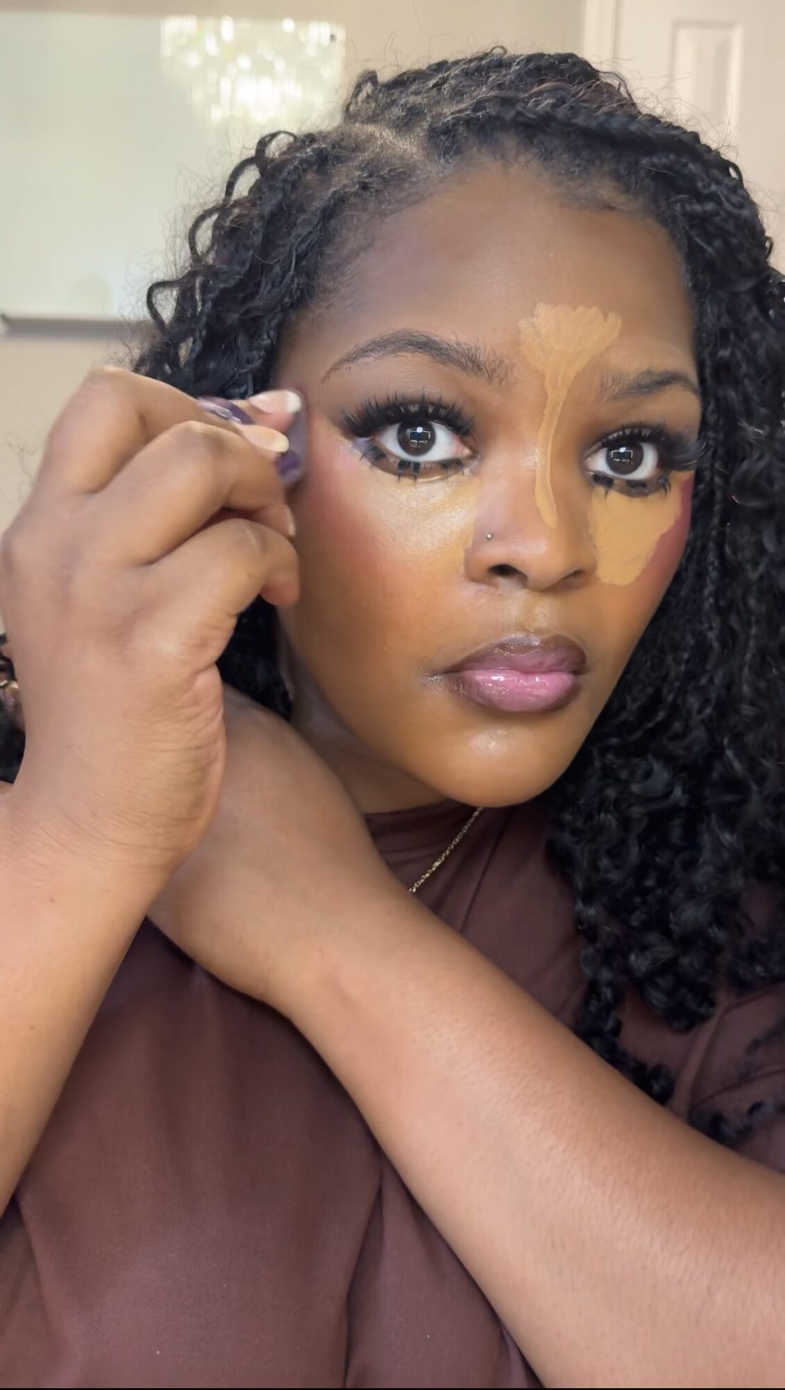 Woman applying makeup with a brush, looking at the camera, with a neutral background.
