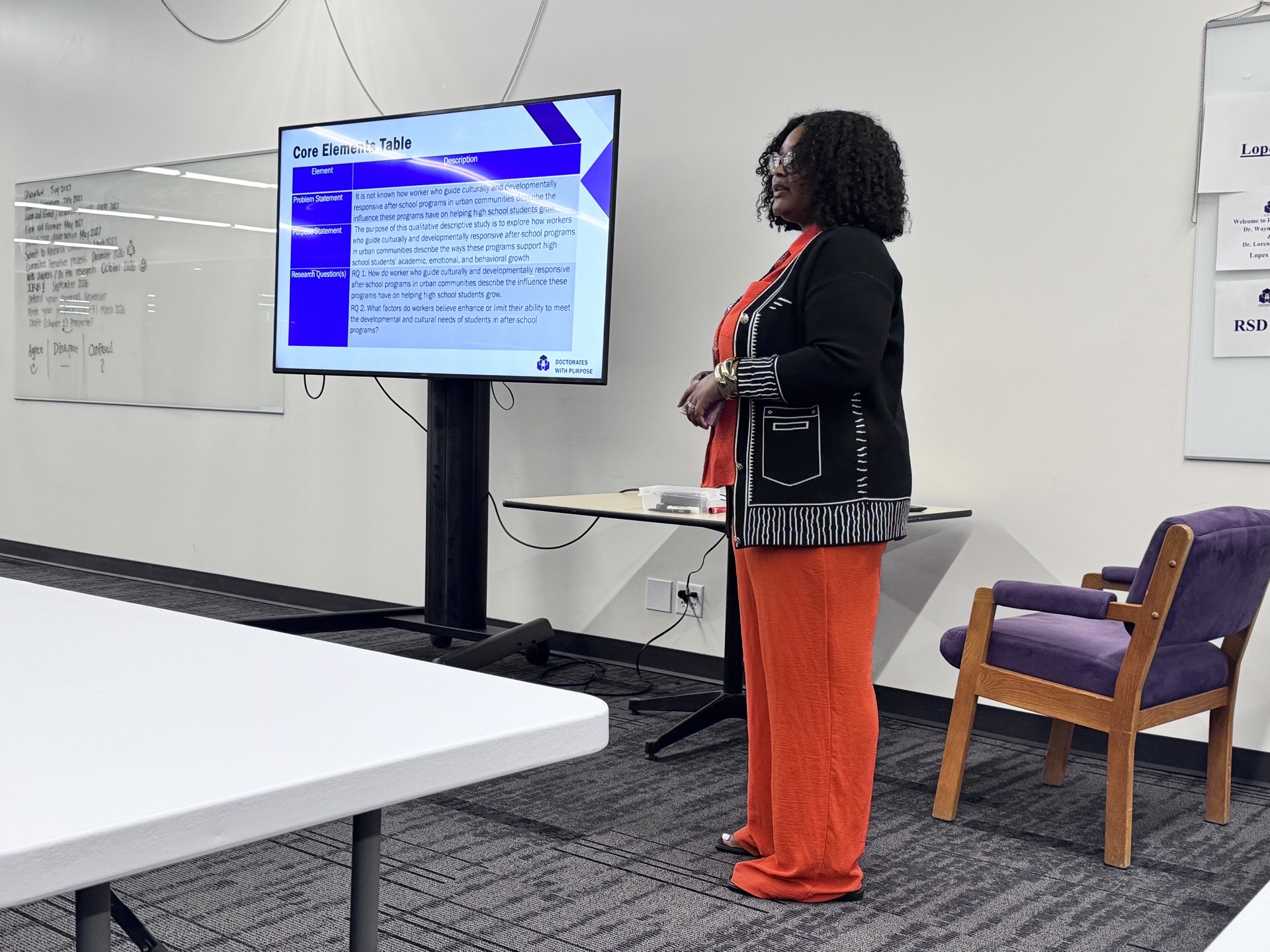 Woman standing in front of a presentation screen, with chairs and whiteboard in background.