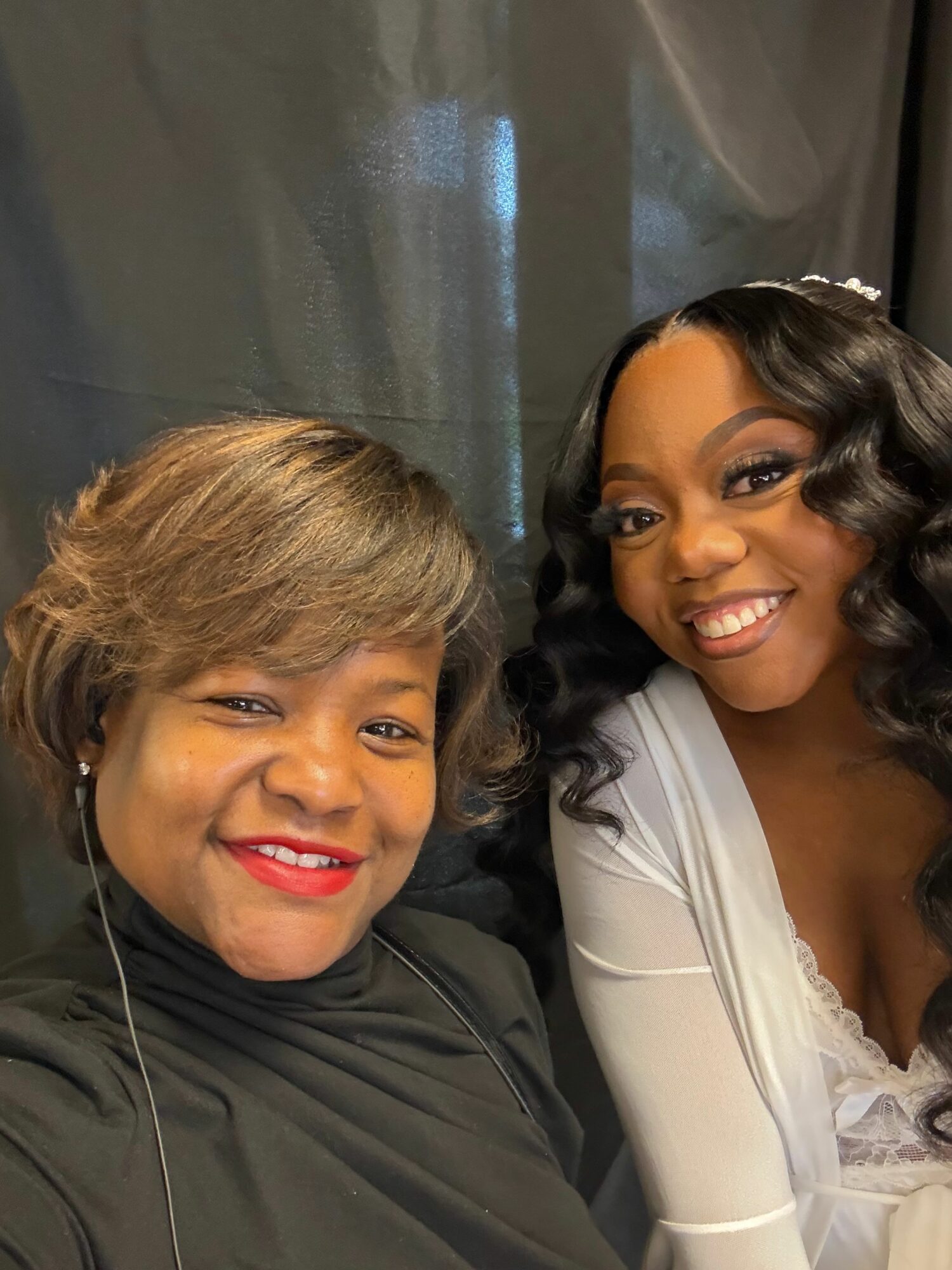 Two women smiling, one with dark hair and the other with light brown hair, close together indoors.