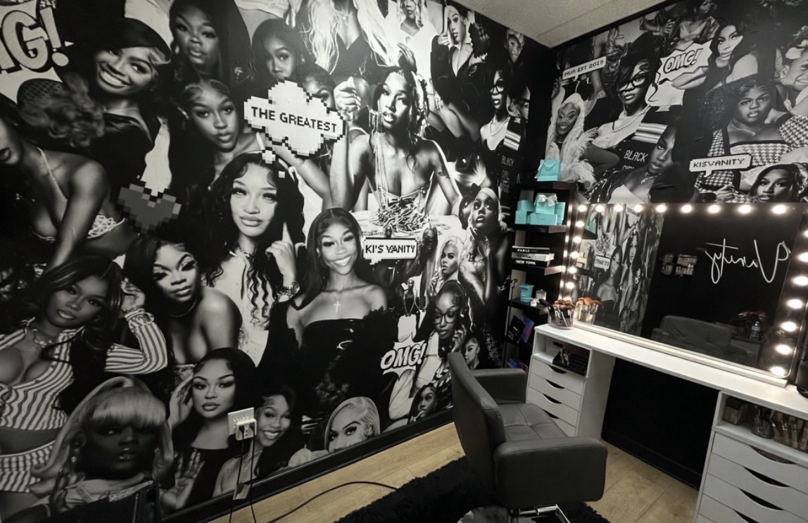 Wall covered with black-and-white photos of diverse women, some holding signs, in a room with a desk and chair.