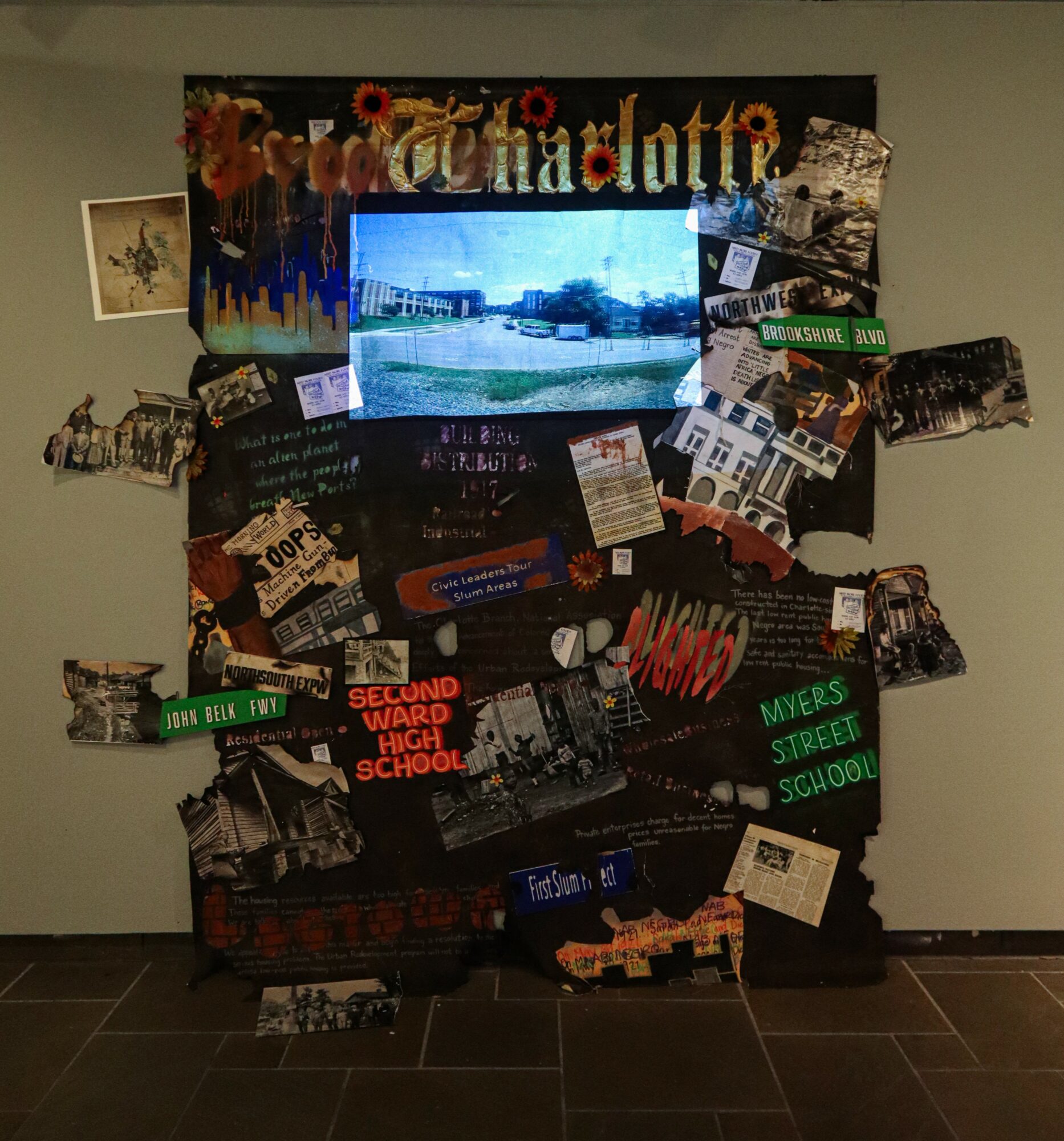 Collage display with a TV screen, photos, and text about a high school, on a wall with a tiled floor.