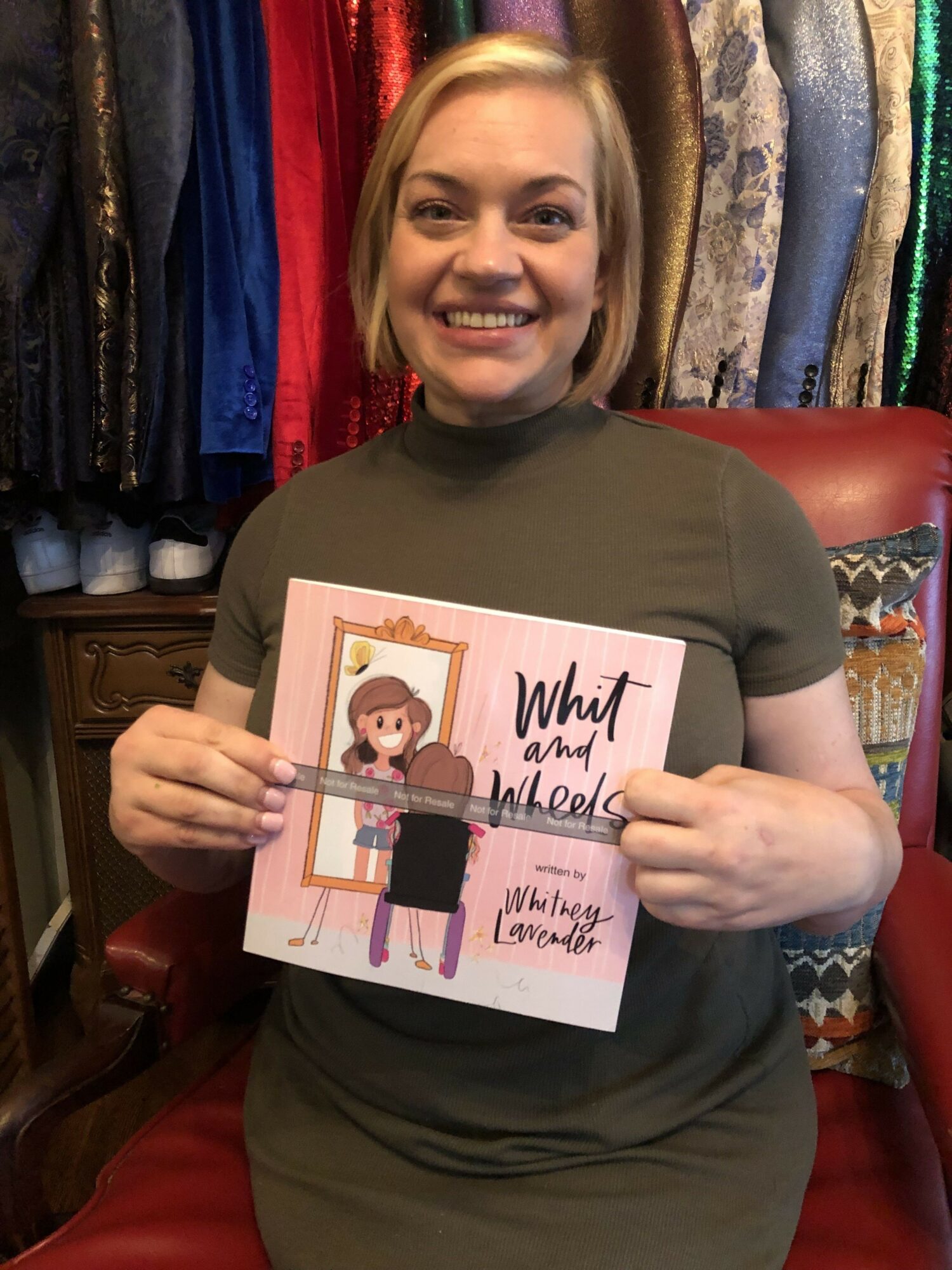 Woman smiling, holding a book titled 'What if I told you I love you' in a store with colorful fabric rolls behind her.