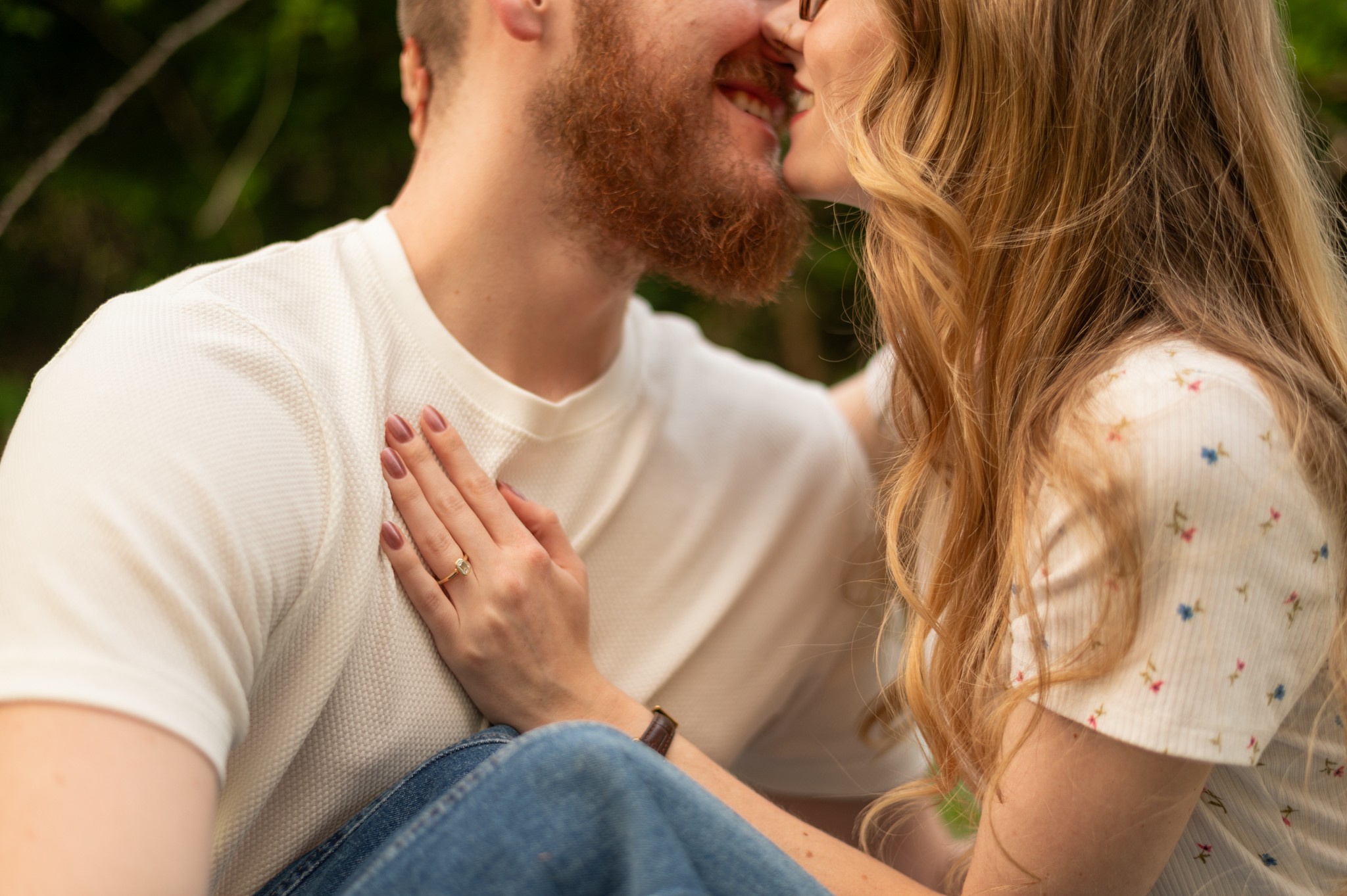 Close-up of a couple with their faces near each other, smiling, outdoors, woman touching man's chest, blurred background