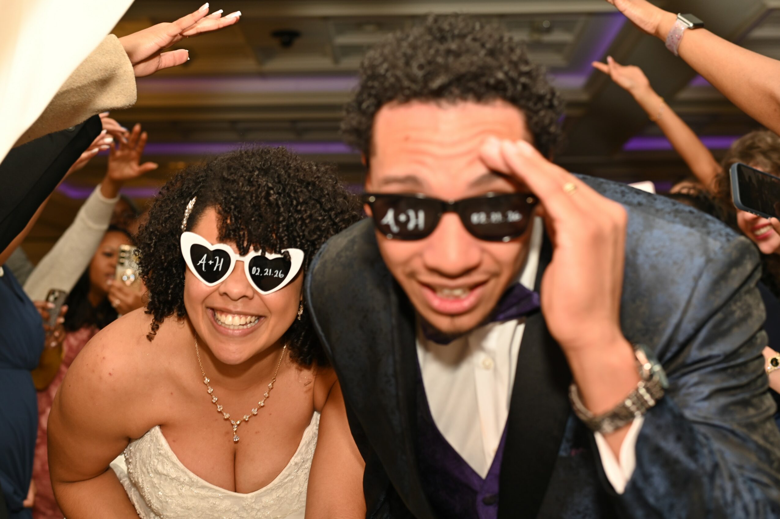 People dancing at a party, wearing sunglasses, smiling, with arms raised in celebration.
