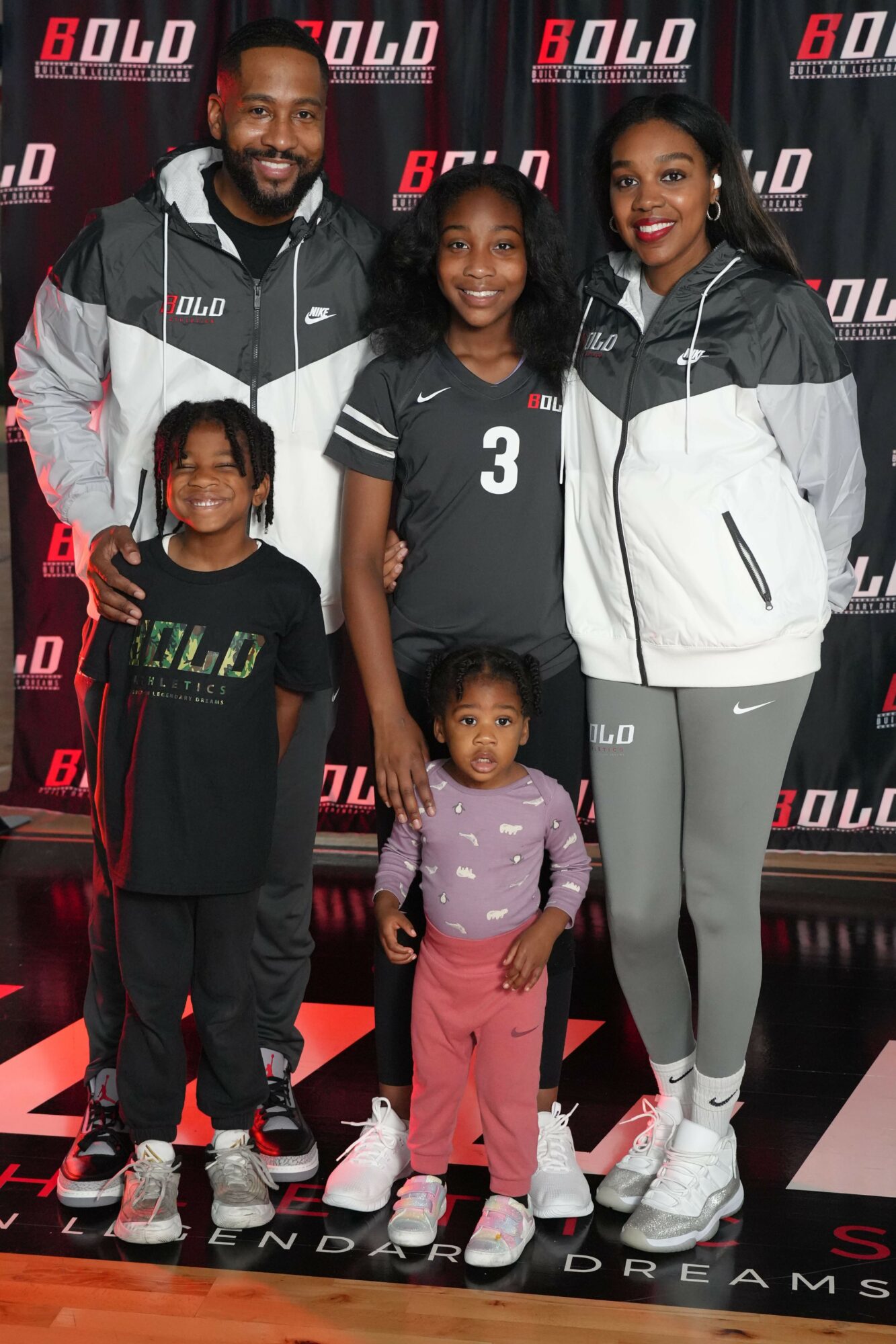 Group of five people standing together on a stage with a red and black background, smiling and posing for the photo.