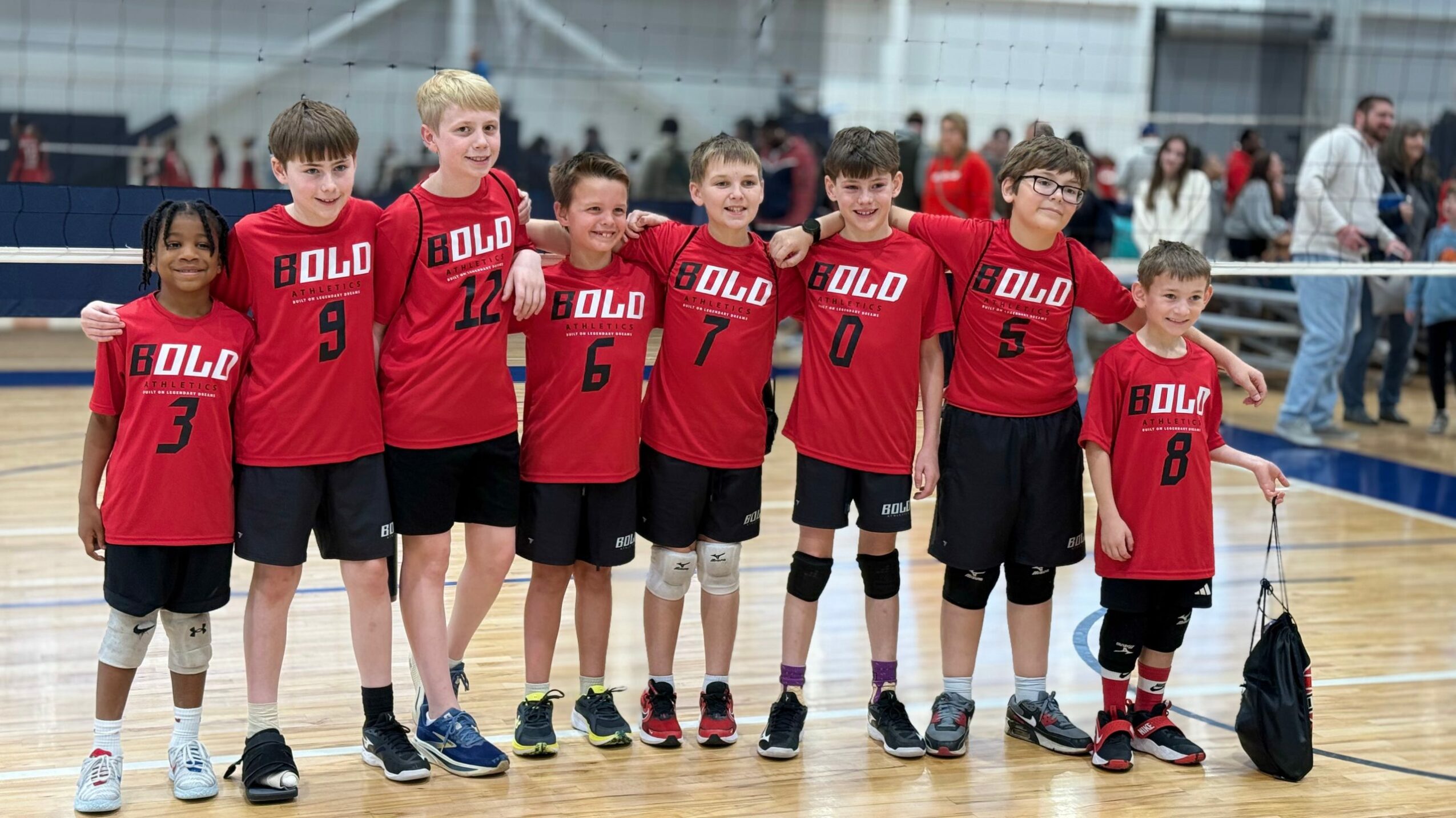Group of young boys in red and black sports uniforms standing on a basketball court, posing for a photo.
