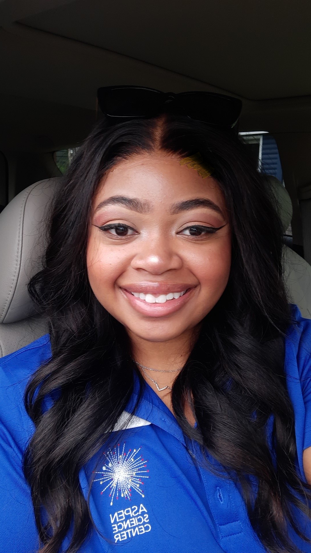 Smiling woman with long dark hair in a blue shirt inside a vehicle.