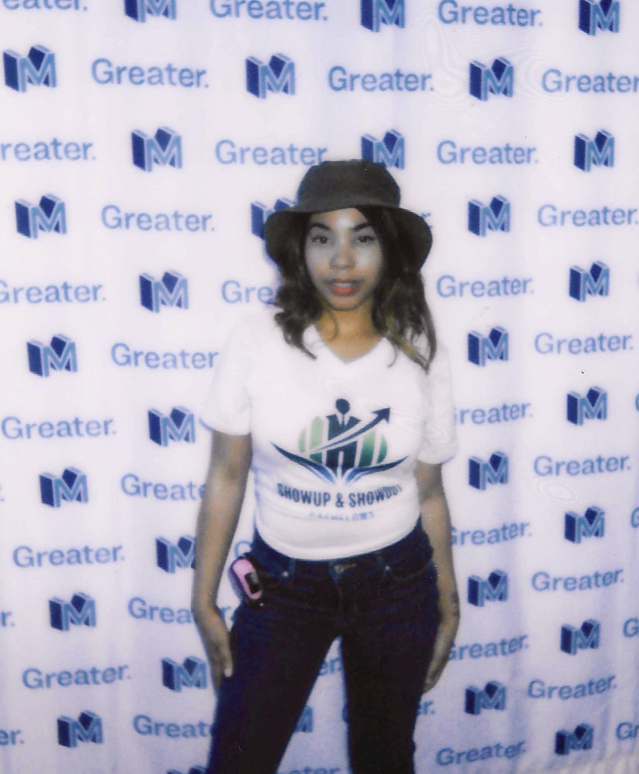 Young woman with curly hair wearing a hat and white T-shirt, standing in front of a blue and white patterned backdrop.