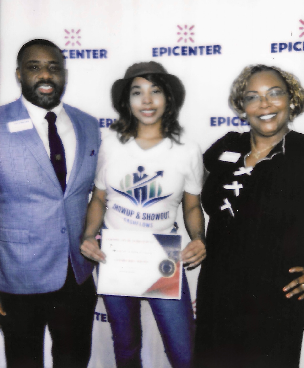 Three people standing in front of a backdrop with 'EPICENTER' logos, smiling, holding a certificate, two women and one man.