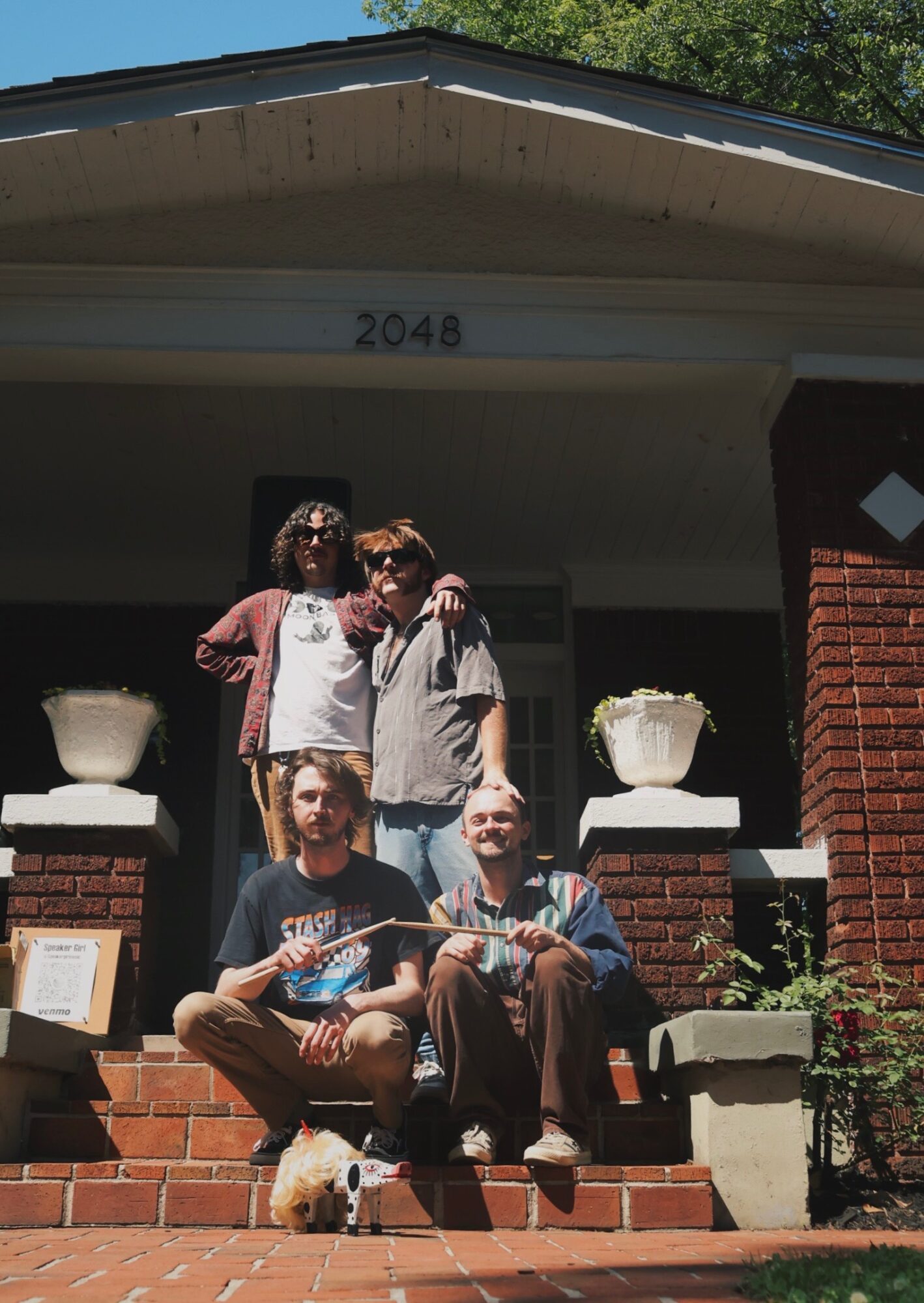 Four people sitting and standing on front steps of a house with the number 2048, two large planters, and brick columns.