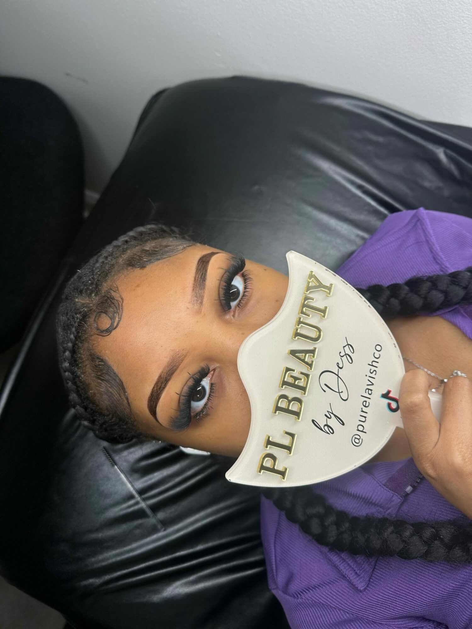 Upside-down image of a young girl holding a sign, with braided hair and a purple top, lying on a black surface.