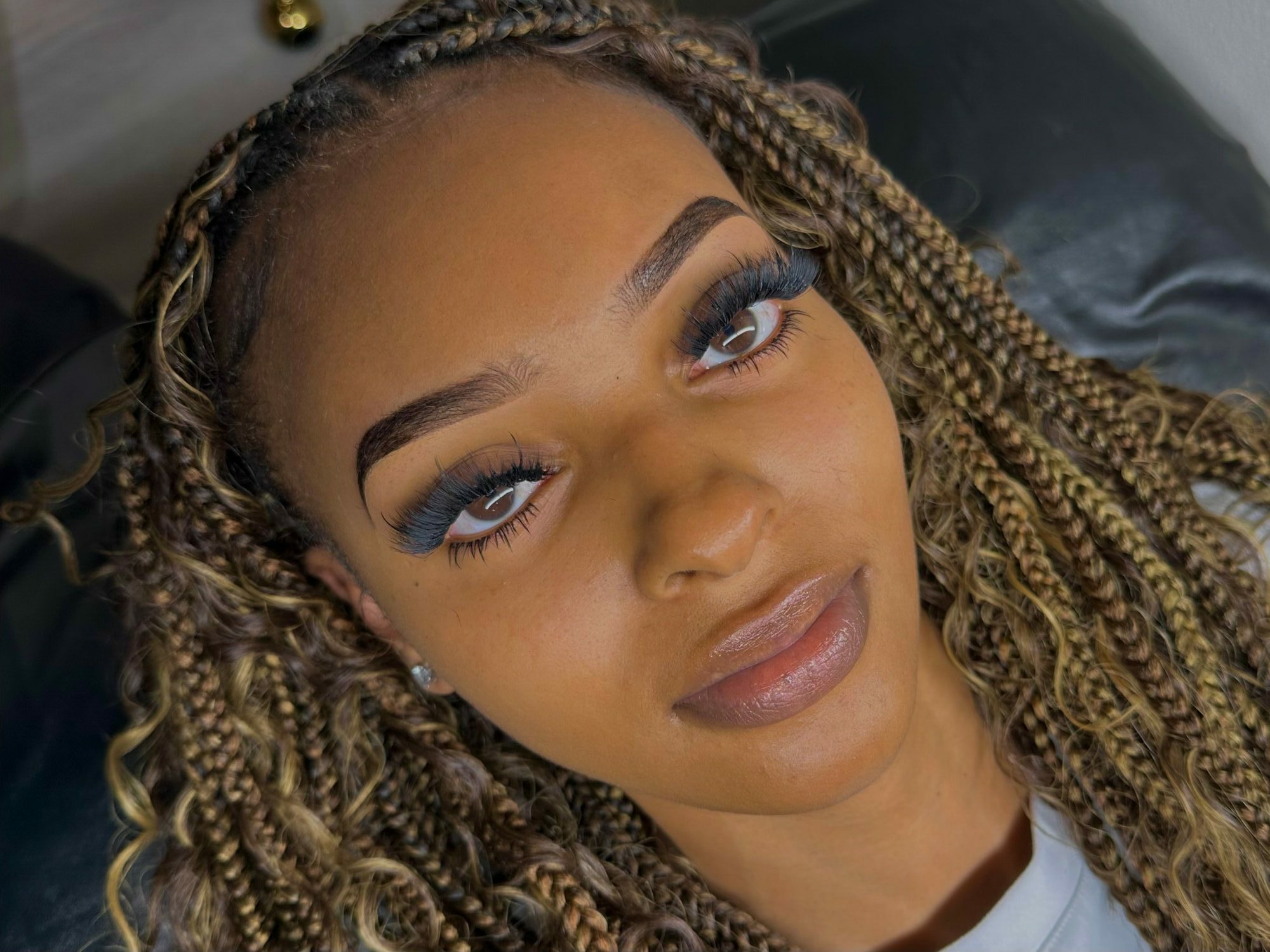 Close-up of a woman with braided hair, makeup, and a neutral expression, lying down with her head tilted.