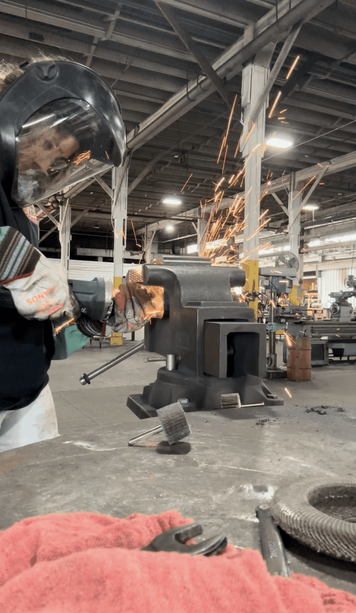 Person wearing protective gear welding metal with sparks flying in an industrial workshop.