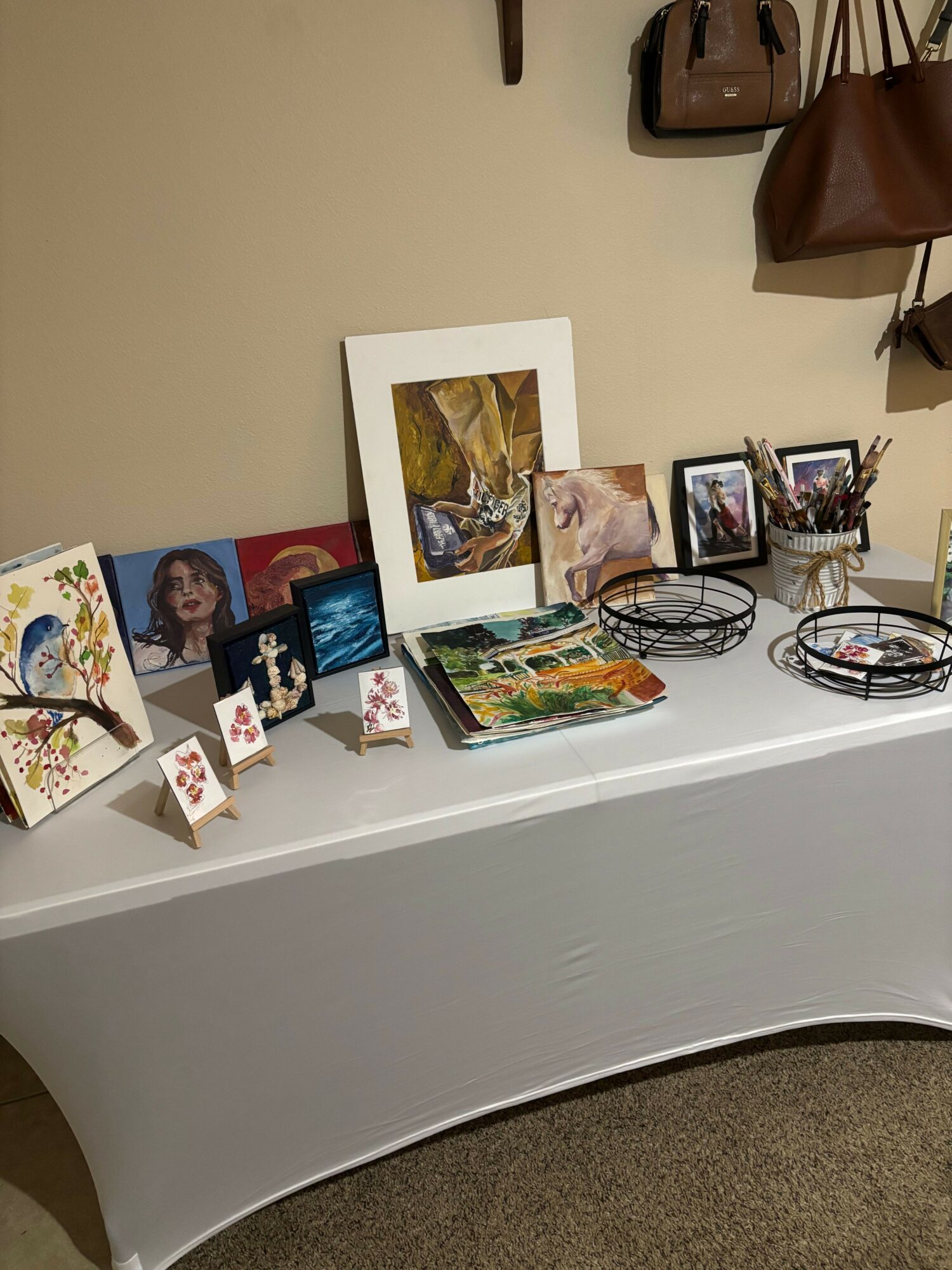 Display table with framed photos, artwork, and decorative items against a beige wall.