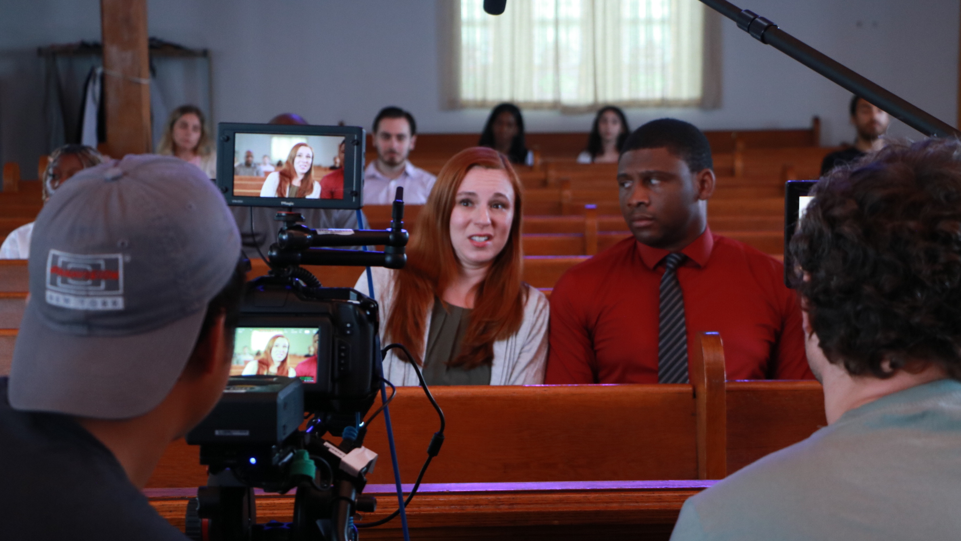 People filming a woman and a man speaking in a courtroom, with camera equipment visible.