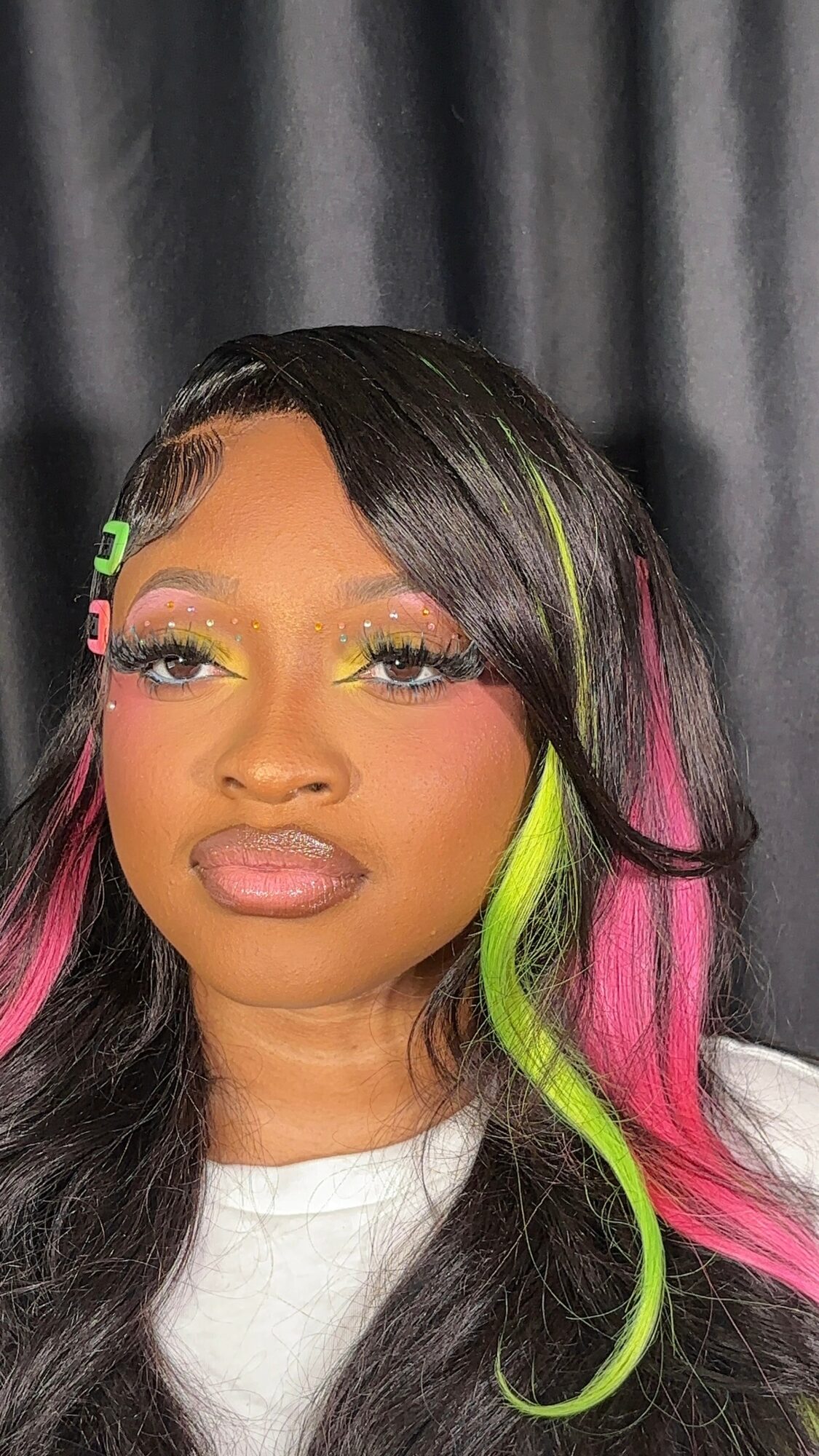 Close-up of a woman with colorful makeup and long, multicolored hair, against a dark background.