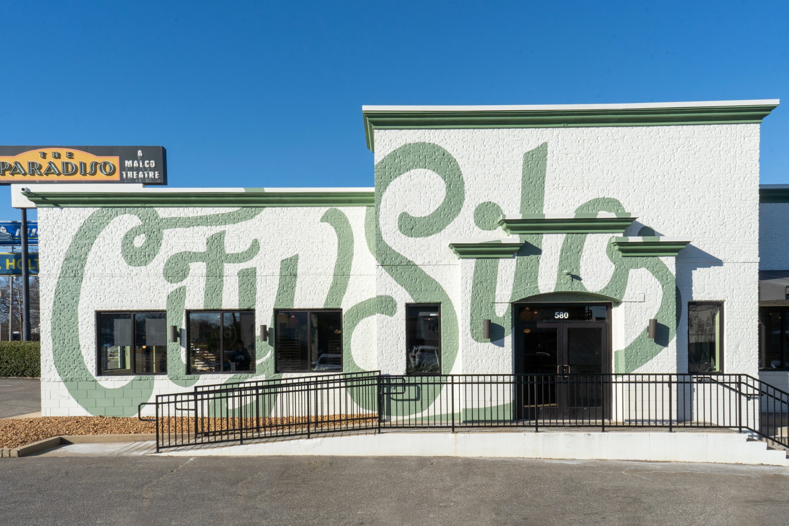 Building with a green decorative pattern on white wall, black door, and windows, with a railing in front.