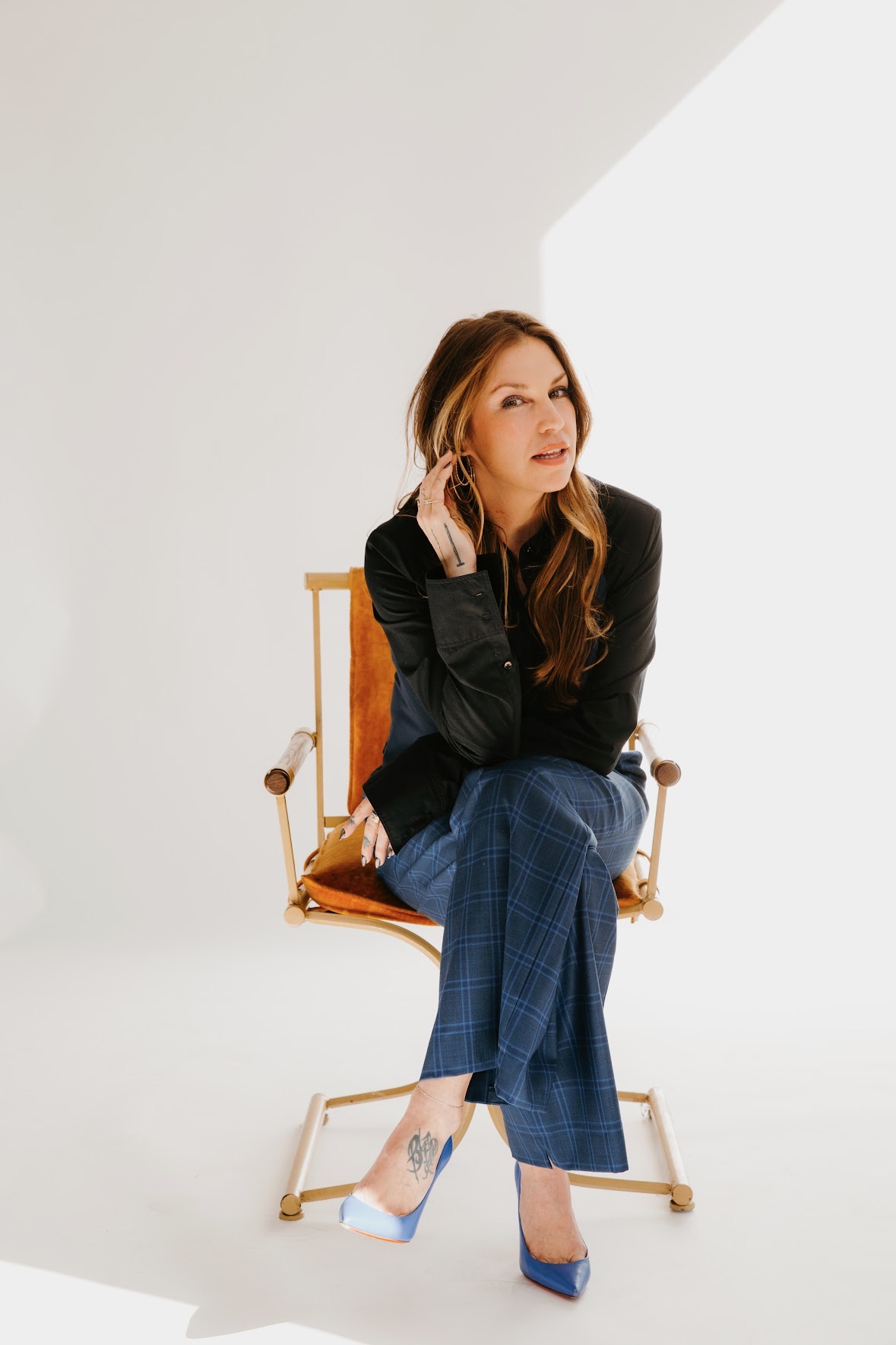 Woman with long hair sitting on a chair, wearing a black top and blue pants, looking to the side.