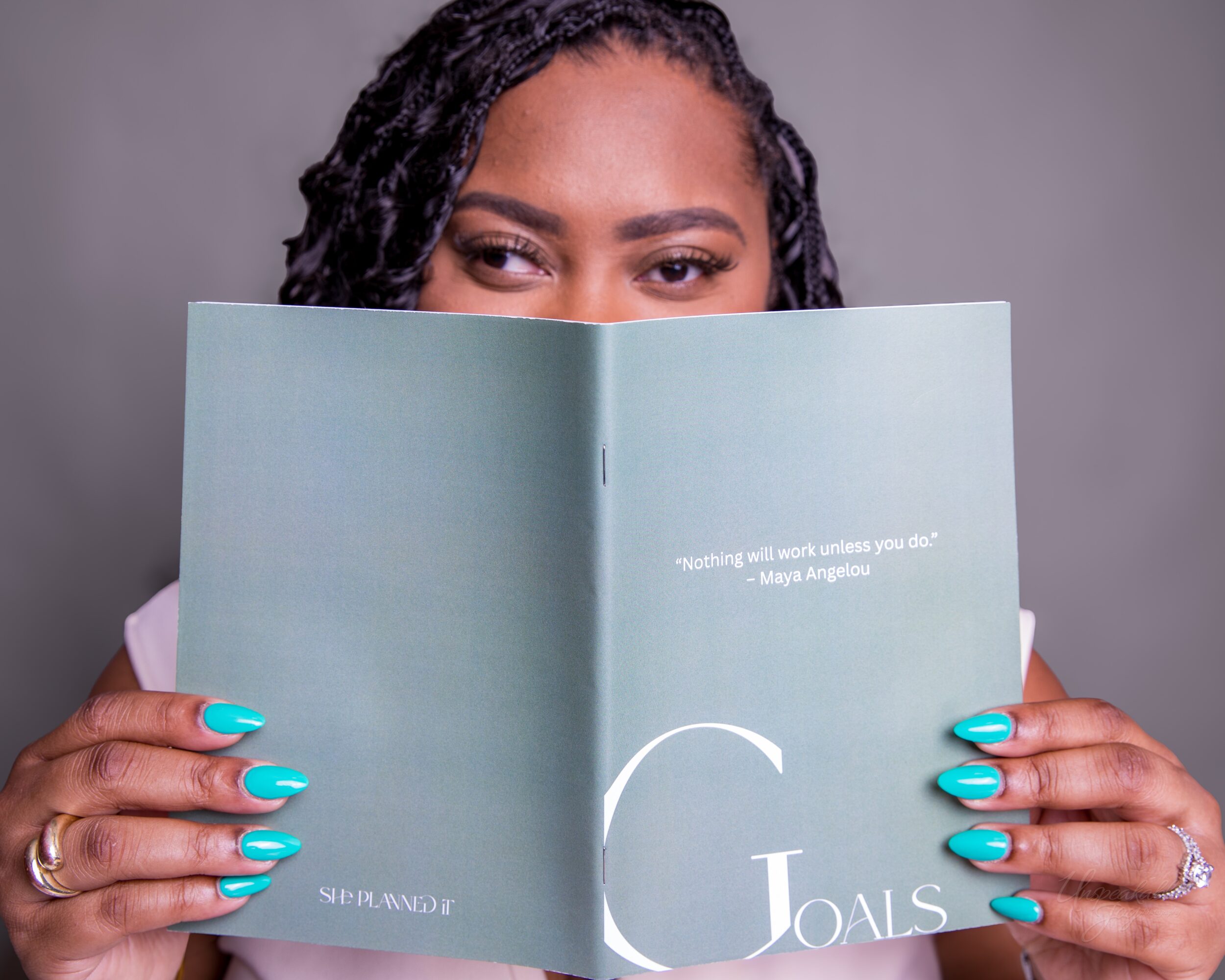Person with braided hair holding an open book with turquoise-painted nails.