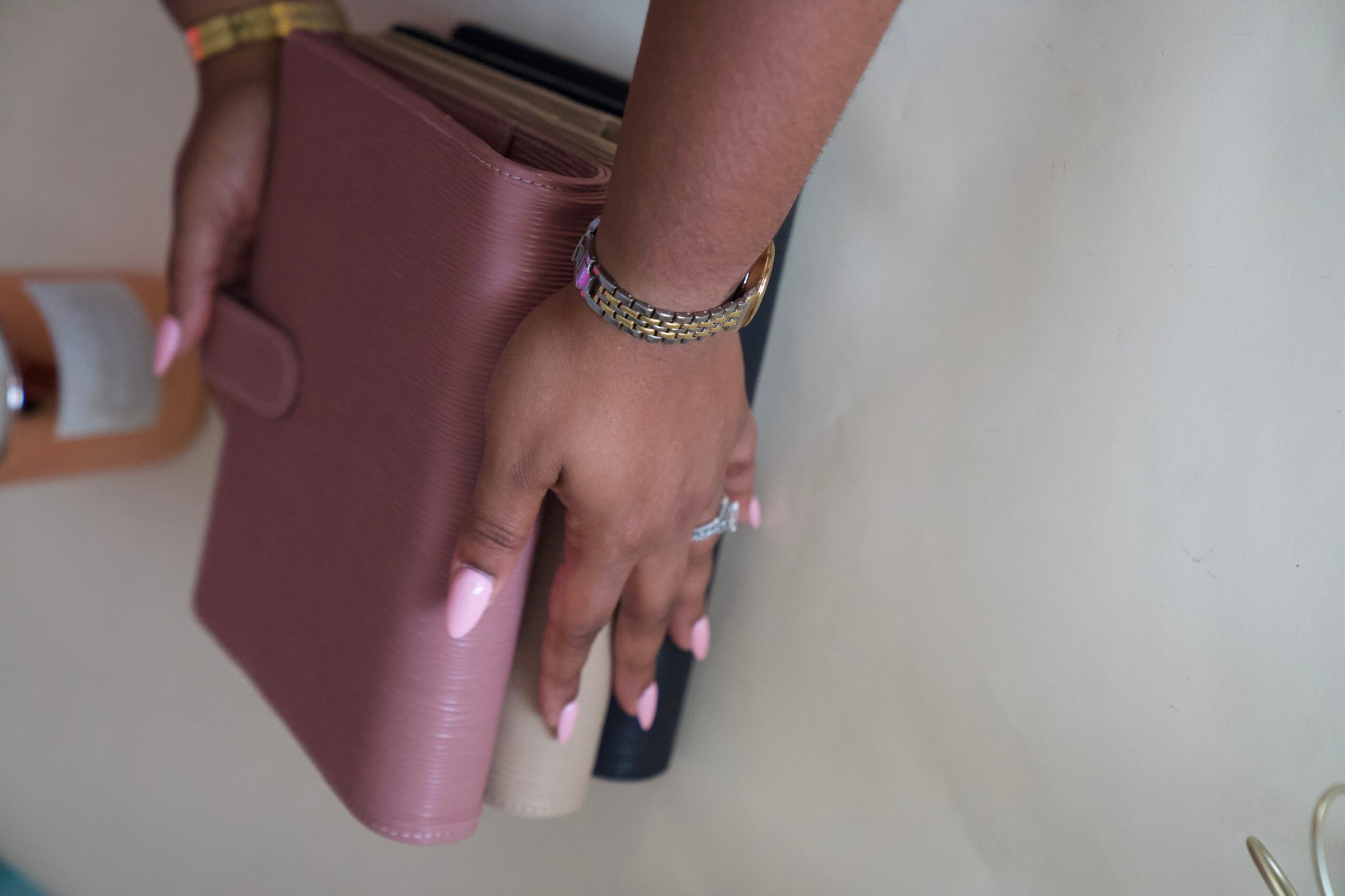 Hands holding a pink wallet beside pens on a light-colored surface.
