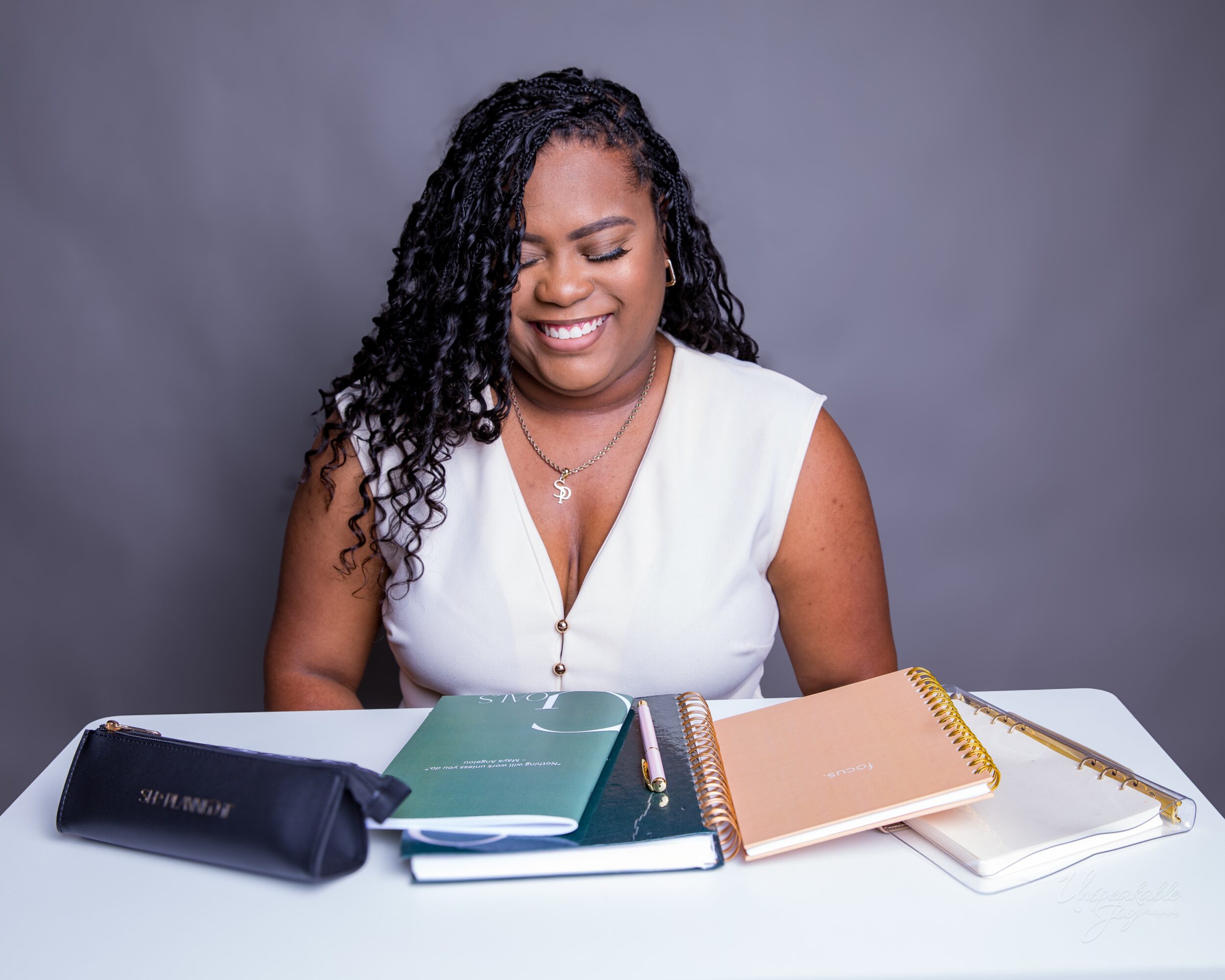 A person smiles at a table with several notebooks and a pen.