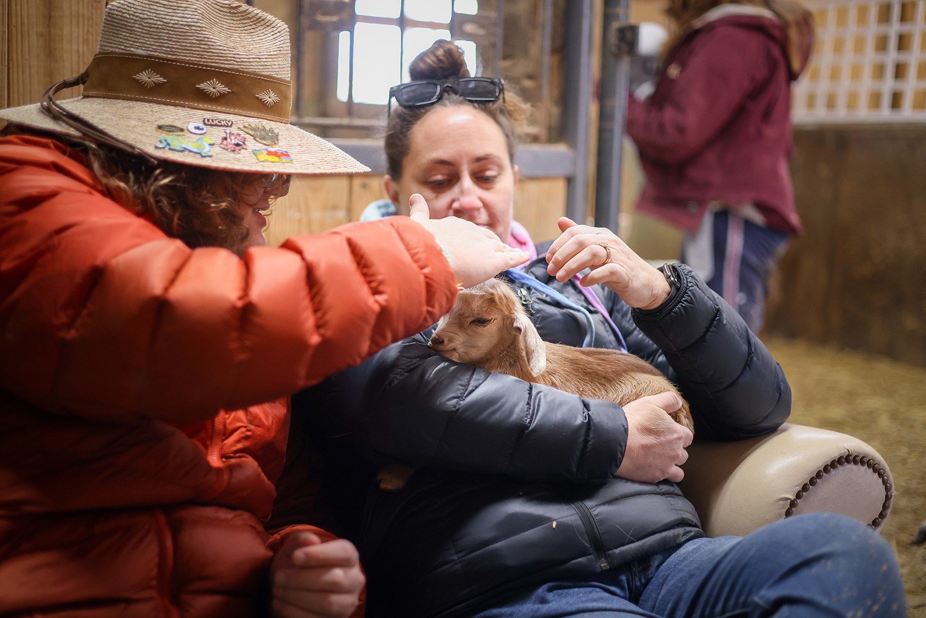 Two people sit together as one holds a small animal; another person stands in the background.